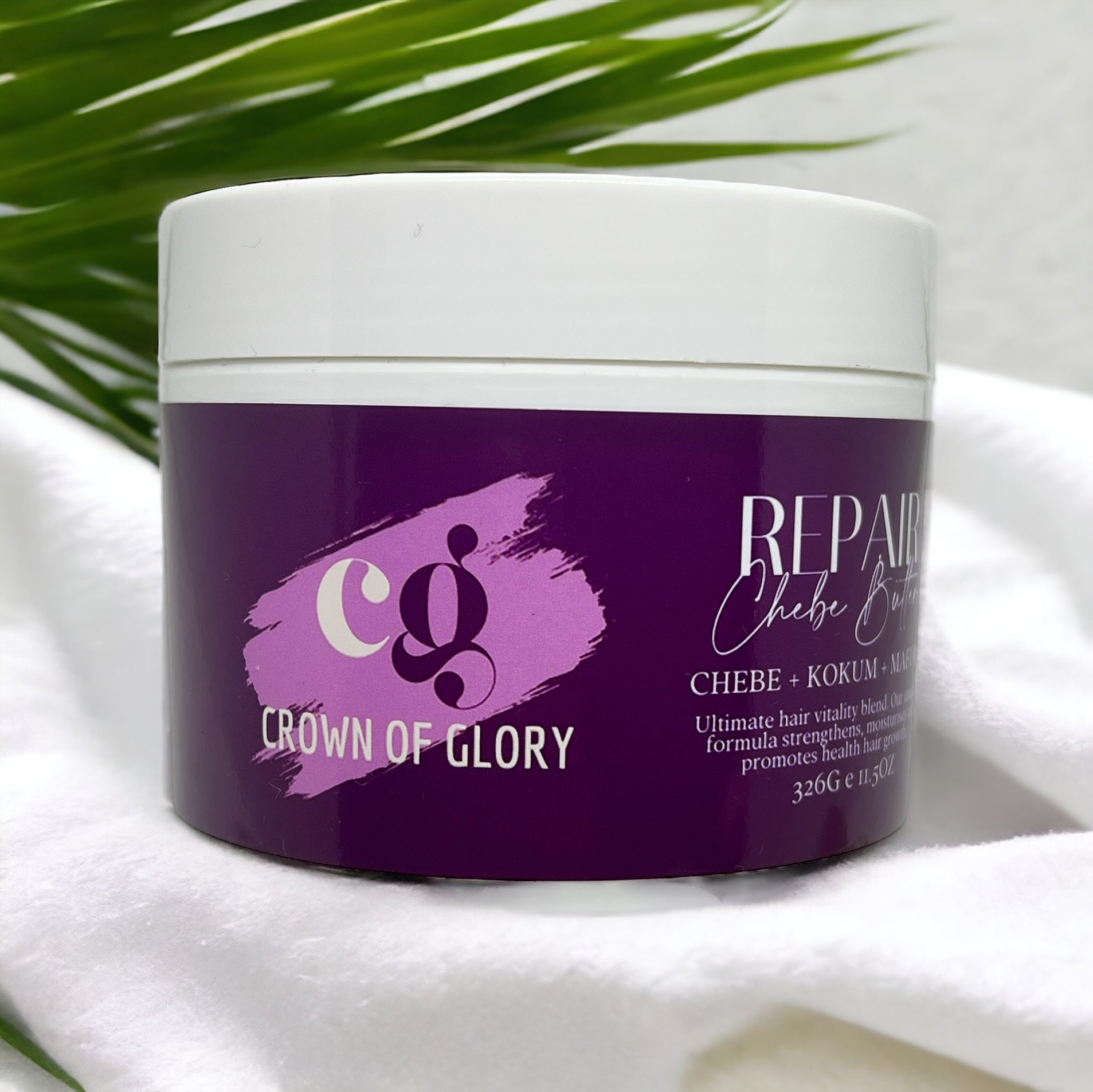 Against a blurred backdrop with green palm leaves, a white cylindrical container prominently displays its purple label. The brand "Crown of Glory" is featured on the label, which highlights "REPAIR" and lists key ingredients: Chebe Butter, Kokum, and Argan. It emphasizes ultimate hair vitality and strength benefits, making it ideal for natural hair care and promoting hair growth. This product is named Repair Chebe Butter – Hair Growth & Nourishing Treatment.